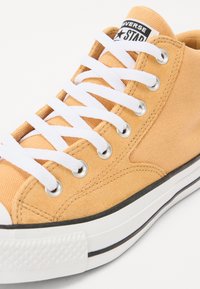 Orange kanvas sneakers med vita snören, kontrasterande svart sula och rund tå. Har en svart och vit logopatch på tungan.