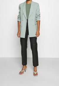 Světle zelený dvouřadý blazer s vycpávkami na ramena, kombinovaný s černými kalhotami z umělé kůže a mentolovými lodičkami na vysokém podpatku.