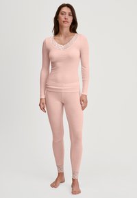 Lichtroze geribbelde longsleeve top met een V-hals afgewerkt met kant en bijpassende legging met kantaccenten op de enkel. Zacht materiaal, getailleerd design.