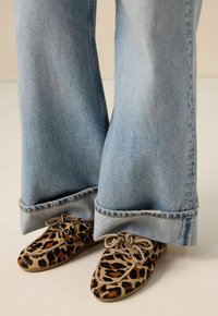 Chaussures à imprimé léopard avec bout rond et fermetures à lacets, associées à un jean pattes d'éléphant bleu clair avec des ourlets effilochés.