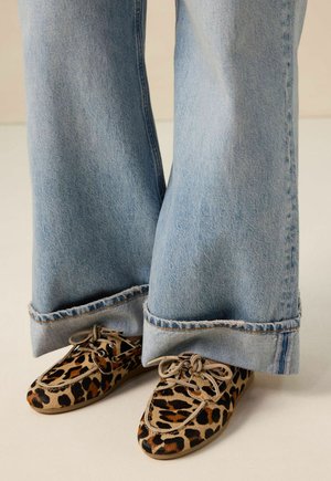 Schuhe mit Leopardenmuster, runden Zehen und Schnürungen, kombiniert mit hellblauen Schlagjeans mit fransigen Säumen.