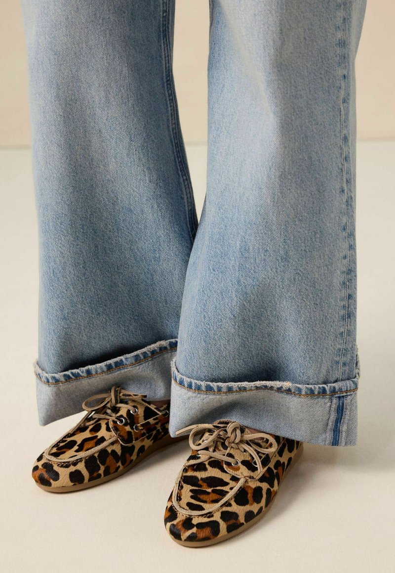 Chaussures à imprimé léopard avec bout rond et fermetures à lacets, associées à un jean pattes d'éléphant bleu clair avec des ourlets effilochés.