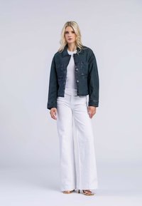 Donkergroene denimjas met knoopsluiting en voorzakken, gecombineerd met een witte ribbeltop en witte broek met wijde pijpen. Eenvoudig ontwerp, geen patronen.