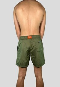 Costumi da bagno verdi realizzati in materiale leggero con una cintura elastica. Presentano tasche e un'etichetta arancione sul retro.