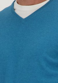 Blauwe V-hals trui gemaakt van zachte brei stof, met een fijne textuur en een subtiele logodetail nabij de halslijn.