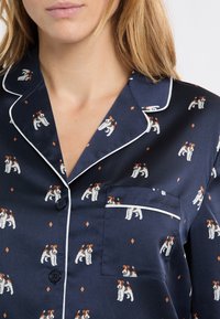 Granatowy satynowy top do piżamy z białym lamówką, ozdobiony nadrukiem psa i diamencikami. Posiada kieszonkę po lewej stronie.