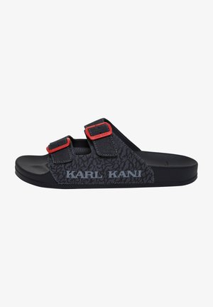 Sandale noire à semelle plate avec deux brides réglables dotées de boucles rouges et du logo "KARL KANI" sur un panneau latéral texturé à motif.