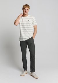 Wit gestreept t-shirt met korte mouwen en een ronde hals, gecombineerd met donkergrijze slim-fit broek en lichte sneakers met een gestructureerde zool.