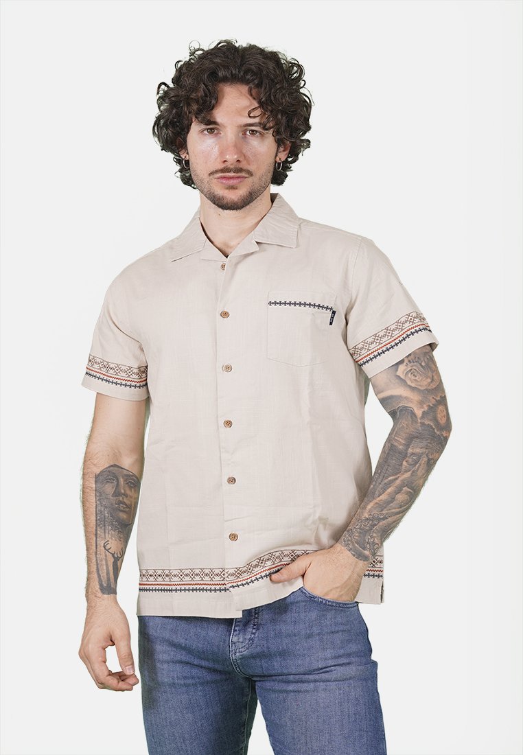 Camicetta beige a maniche corte realizzata in tessuto texturizzato, con bottoni marroni e maniche decorate con un motivo. Inclusa tasca frontale.