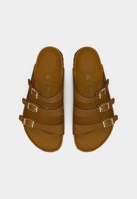 Καφέ σανδάλια με τρεις ρυθμιζόμενους ιμάντες και χρυσά αγκράφες. Κατασκευασμένα από λείο, ανθεκτικό υλικό με ελεύθερο πέλμα που ακολουθεί τη φόρμα του ποδιού.