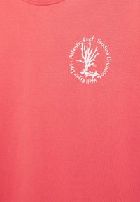 T-shirt rose corail avec un logo circulaire blanc présentant une illustration de corail et le texte « Atlantic Reef Studies Division, Well River Dpt. »