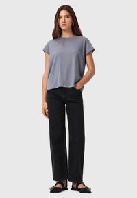 Camiseta gris de manga corta con un ajuste relajado, combinada con unos pantalones vaqueros de pierna recta negros de cintura alta y zapatos planos negros. Diseño simple, textura suave.