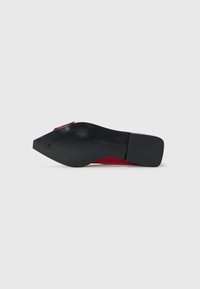 Semelle noire d'une chaussure rouge pour femmes à bout pointu avec un petit talon carré, nom de la marque "Steve Madden" visible sur la semelle.