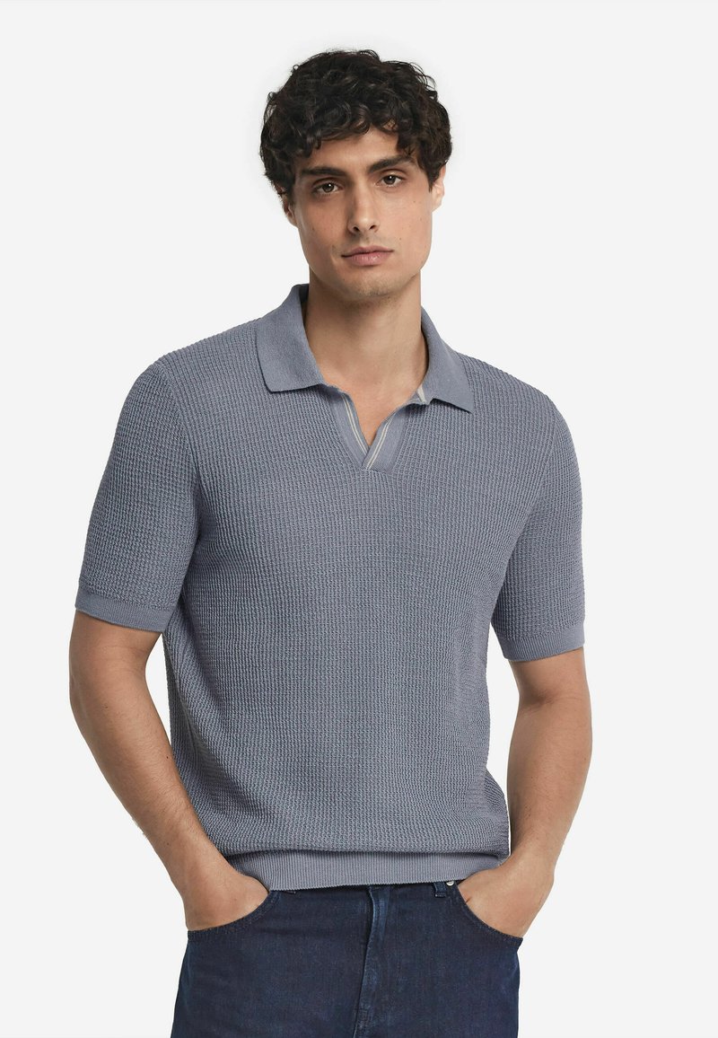 Kortärmad polo skjorta i ljusblått texturerat stickat tyg, med kollared hals och en partiell knäppning. Avslappnad passform.