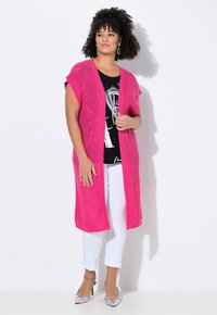 Rosa offen gestrickte Strickjacke über einem schwarzen Grafikshirt, kombiniert mit weißen Hosen und silbernen Absätzen. Verfügt über kurze Ärmel und eine lässige Passform.