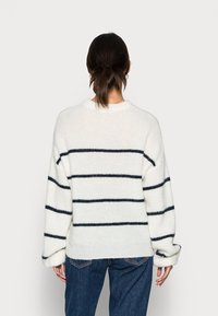 Pull en maille épaisse crème à rayures horizontales bleu marine, col rond, épaules tombantes, et détails côtelés au niveau des poignets et de l'ourlet.