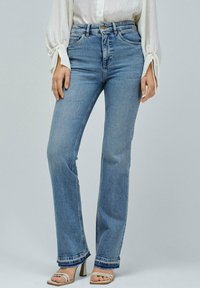 Jeans de tiro alto en azul claro con un corte recto, que presentan un dobladillo deshilachado, costuras en contraste y un diseño clásico de cinco bolsillos.
