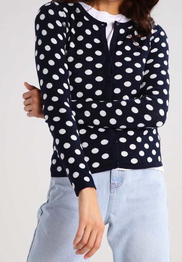 Navy cardigan with white polka dots, round neckline, long sleeves, and button closure, paired with light blue jeans.