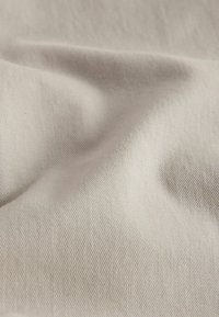 Tessuto beige morbido con texture sottile di tessitura diagonale e pieghe delicate che creano variazioni di luce e ombra.