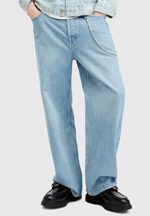 Light blue wide-leg jeans made of denim, featuring a silver chain accent and slight fading, styled with black shoes.