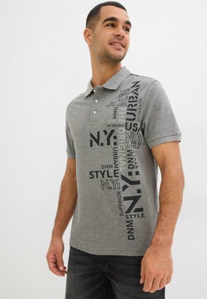 Polo grigio con patta a due bottoni, maniche corte e una grafica stampata che presenta un testo in nero e grigio scuro.
