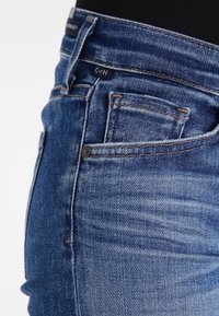 Mörkblå denimjeans med slim fit, med en femfickdesign, kontrastsömmar och synliga slitage-mönster.