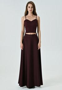 Completo bordeaux a due pezzi composto da un top cropped attillato con spalline sottili e una lunga gonna fluida, realizzato in un tessuto liscio e strutturato.