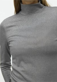 Haut turtleneck gris à côtes avec une silhouette ajustée, fabriqué en tissu métallique texturé qui reflète la lumière et possède des manches longues.