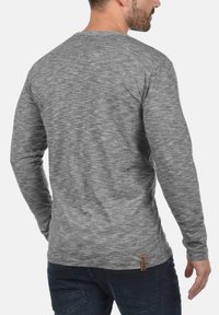 Grau, langärmliges Shirt aus strukturiertem Stoff, mit Rundhals, eng anliegenden Ärmeln und einem kleinen Etikettakzent am Saum.