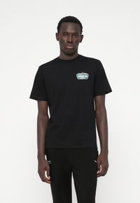 Črna bombažna majica s kratkimi rokavi, ki na levem prsnem delu prikazuje majhno, večbarvno grafiko "CLOSURE LDN". Ima okroglo ovratnico.