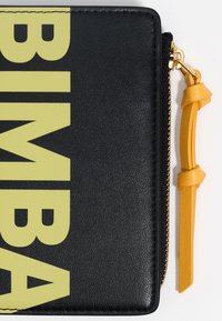 Cartera de piel negra con grandes letras amarillas "BIMBA." Presenta un cierre de oro y un acento de tirador de cuero amarillo. La textura es suave.