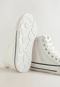Witte canvas high-top sneakers met een gestructureerde witte rubberen zool featuring pizza- en koekjespatronen, vetersluiting aan de voorkant en een rits aan de zijkant.