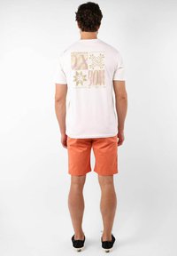 T-shirt en coton blanc avec un design graphique multicolore au dos, associé à un short orange et des chaussures noires à enfiler.