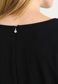 Svart klänning i ett mjukt tyg, med rund halsringning och en diskret dragkedja baktill. Rena, minimalistiska linjer.