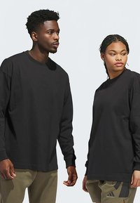 Camisetas de manga comprida pretas em dois modelos. Feitas de tecido macio, com gola redonda e corte descontraído. Ambas combinadas com calças cáqui.