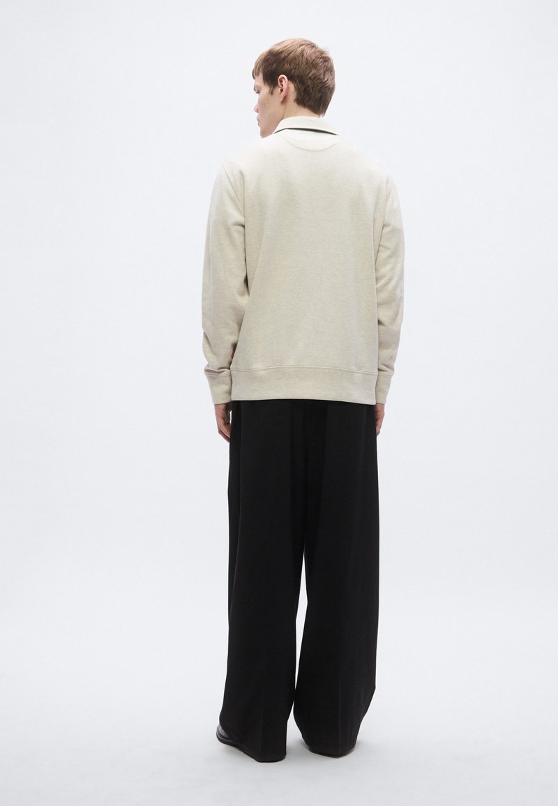 Beige sweatshirt with ribbed cuffs and hem, paired with wide, black trousers. Simple design, soft texture, and relaxed fit.