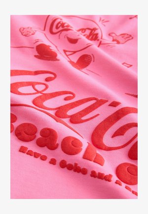 Pink fabric featuring a repeating red Coca-Cola logo and text, with a smooth texture and bold, retro-style lettering.