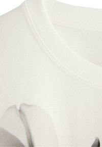 Hvid bomulds t-shirt med rund hals, synlige sømme og et trykt gråt blomstermønster på forsiden.