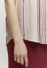 Chemise à manches longues à rayures en tissu léger, comportant des rayures verticales dans des tons de rose doux, lavande et crème. L'ourlet est légèrement arrondi.