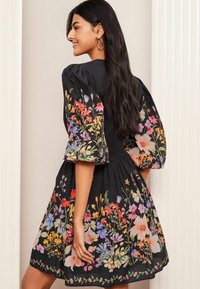 Robe noire avec une broderie florale éclatante de plusieurs couleurs, manches courtes bouffantes et coupe décontractée. Tissu lisse, longueur genoux.