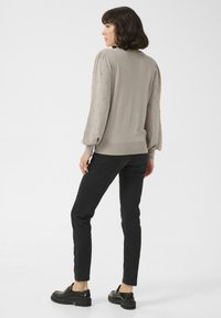 Hellgrauer Pullover mit strukturierten Puffärmeln, versehen mit kleinen dekorativen Elementen. Kombiniert mit schwarzen, schmal geschnittenen Jeans und klobigen schwarzen Schuhen.