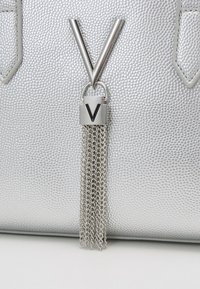 Sac à main argenté avec une surface texturée, arborant un grand logo "V" argenté et un fermoir métallique suspendu avec des chaînes.