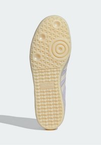 Suela de zapatilla blanca con un patrón de agarre texturizado, que presenta formas circulares y de diamante, con un destacado logo de Adidas en el talón.