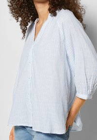 Błękitna i biała koszula w paski na guziki z dekoltem w serek, rękawami 3/4 i luźnym krojem, wykonana z miękkiej, teksturowanej tkaniny.