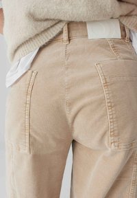 Pantaloni di cotone beige a coste con righe verticali, dotati di ampie tasche posteriori e un'etichetta bianca con marchio in vita.