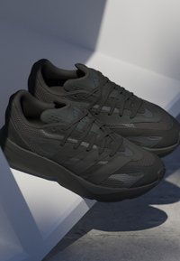 Black athletic shoes feature a mesh upper with textured accents, rubber soles, and multiple lace loops for secure fit.