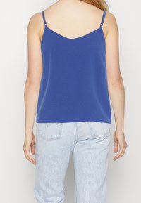Blue cami top with thin straps, a V-neckline, and a relaxed fit. The fabric is smooth and lightweight, paired with light wash denim jeans.