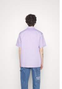 Kortärmad skjorta med krage i ljus lavendel, tillverkad av ett mjukt tyg; har rak nederkant och avslappnad passform.