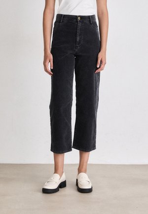 Pantaloni neri a vita alta in denim, cropped, con chiusura frontale a bottone e tasche laterali. Abbinati a mocassini color crema, con suola lavorata.