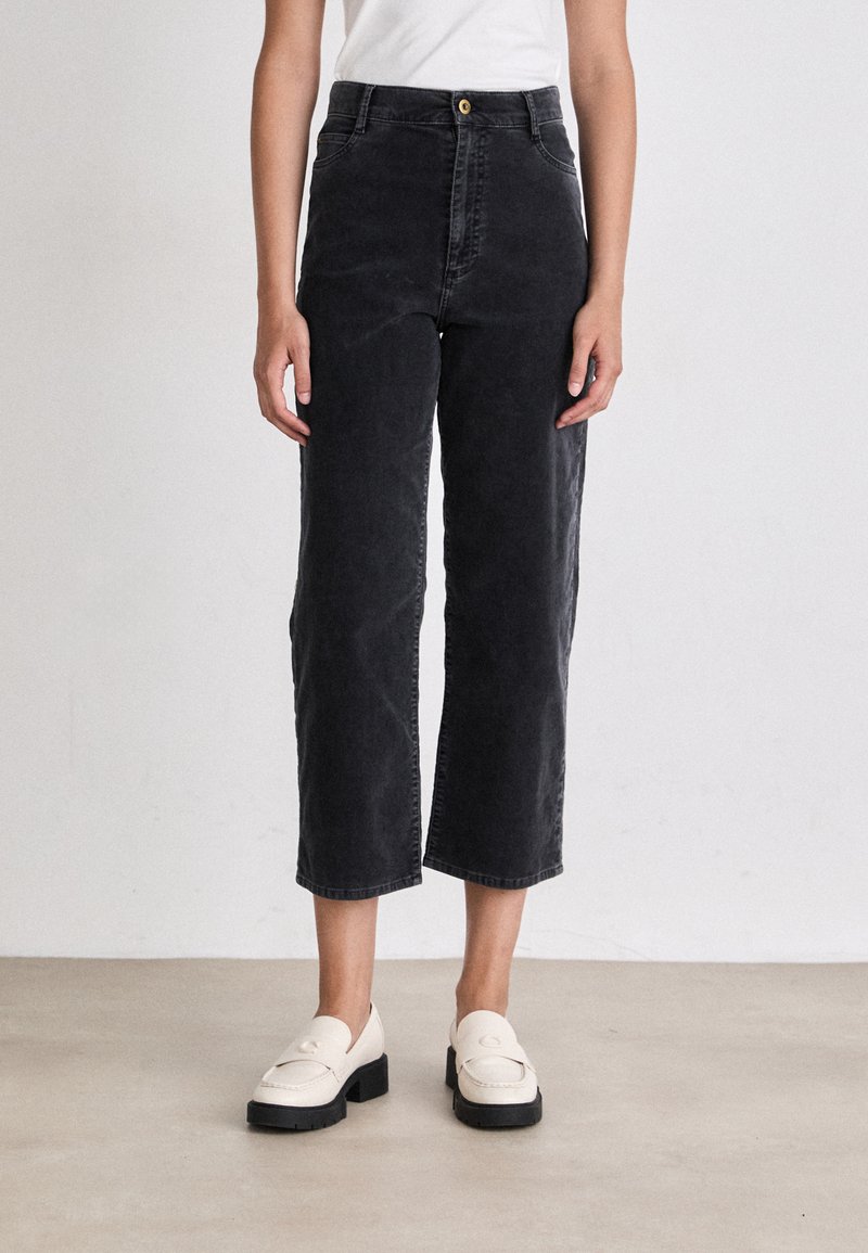 Zwarte cropped broek gemaakt van denim met een hoge taille, voorzien van een sluiting met een knoop aan de voorkant en zijzakken. Gecombineerd met crèmekleurige loafers met een gestructureerde zool.